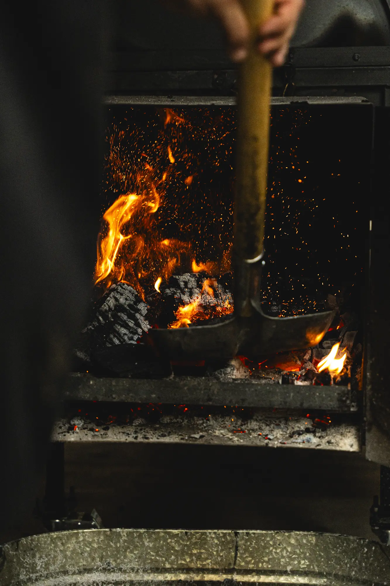 A cook tending glowing coals and open flames in the smokehouse